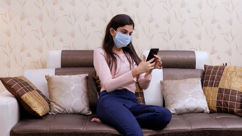Sick Indian female in a surgical mask busy over a video call - lifestyle concept. The beautiful young girl happily doing a video call to her friends during the Covid-19 pandemic time in India