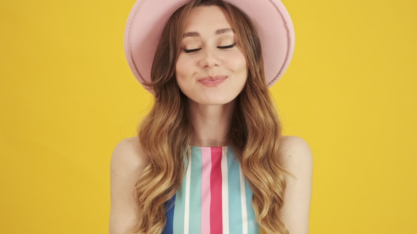 A pretty cute young woman in a pink hat is posing isolated over a yellow background