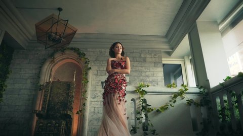 beautiful woman fairy tale queen bride. Princess Girl fashion model in old room castle. Long trendy wedding peach dress decorated with red creative artificial red butterflies. Hair elegant hairstyle