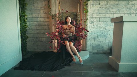 Beautiful fairy tale young woman princess sits on royal throne image art queen butterfly fashion model posing. backdrop interior room castle. Creative carnival halloween costume many red orange moths
