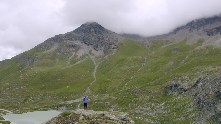 Drone point of view turning around woman on mountain ridge standing arms wide open embracing life and enjoying nature. 
Successful people on top of mountain reaching summit, glacier view, Switzerland 