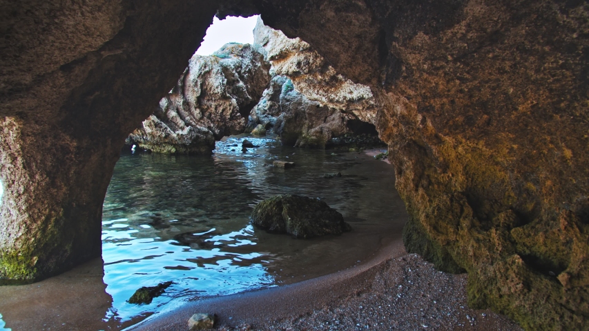 View from small cave on rocky coastline of waves running onto shore, static shot