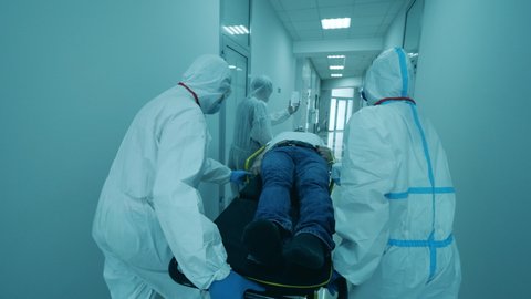 Coronavirus pandemic concept. Physicians in protective suits carry a man on stretcher.