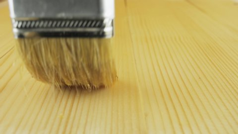 A person varnishes a wooden surface. Wood surface absorbs varnish. Painting wooden surface using a paintbrush. Paintbrush on wood table in close-up.