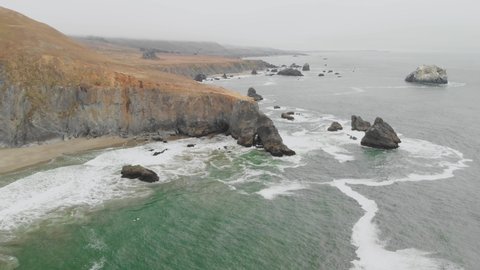 Expansive aerial pan out of a surfer waiting to ride the waves along the Sonoma Coast.