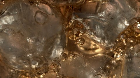 Pouring Cola on ice cubes extreme close-up. Cola with Ice and bubbles in glass in dramatic slowmotion. Coke Soda closeup. Syrupy refreshment beverage. Ice cold drink on a hot summer day. Cocktails
