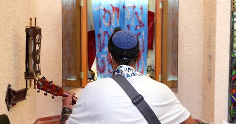 Rabbi of the Jewish Reform movement is wrapped in a Tallit, prays, and plays the guitar in front of the Torah ARK.
