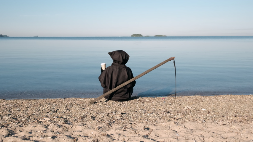 Grim Reaper in a Black Hoodie with a Scythe Sitting by Lake with Cup of Coffee. Slow Motion. Safety on Vacation and Prevention Water Accidents in Summer Concept | Shutterstock HD Video #1056282179