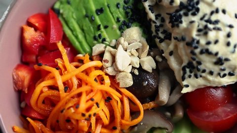 Poke bowl with vegetables and hummus filmed on table from above.Video clip with natural ingredients for healthy eating.Vegetarian breakfast meal prepared with fresh raw products