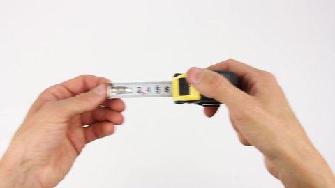 human hands pull the measuring tape out of tape measure and measure the length or width dimensions, then removes from frame, close up view on white background