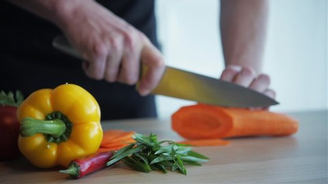 Close up shot of man hands slicing carrot on wooden cutting board.
Man is cutting carrot into small pieces with sharp knife, healthy food, home cooking, diet, diet food, vegetarian food.