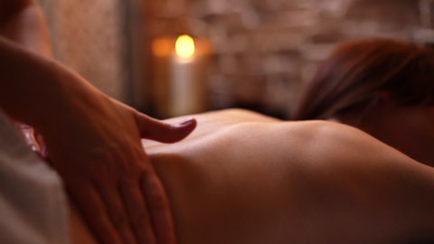 Female masseuse does back massage to young unrecognizable woman in spa centre, close-up. Woman massage therapist performs circular movements to relax back muscles. Shooting in slow motion.