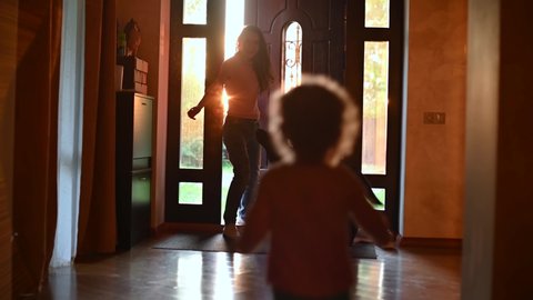 A child meets mom from work. The girl joyfully runs to the front door, where her mother enters, Backlight, camera moves