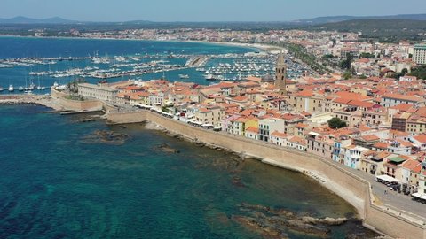 Aerial shot over Alghero old town, cityscape view on a beautiful day with harbor and open sea in view. Alghero, Italy. Panoramic aerial view of Alghero, Sardinia, Italy. 