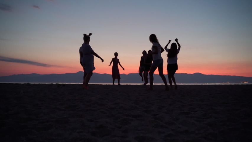 A group of friends dancing barefoot at the sea beach on amazing sunset background, crowd of happy friends having fun at the beach party, celebrating the end of summer holidays and vacation Royalty-Free Stock Footage #1056287612