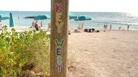 Key West, Florida - December 4, 2019: People tan and rest by a wooden signpost on the sunny beach of Fort Zachary Taylor State Park in tropical Key West Florida USA