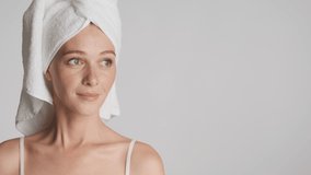 Gorgeous woman with towel on head happily looking aside on copy space and in camera over gray background.