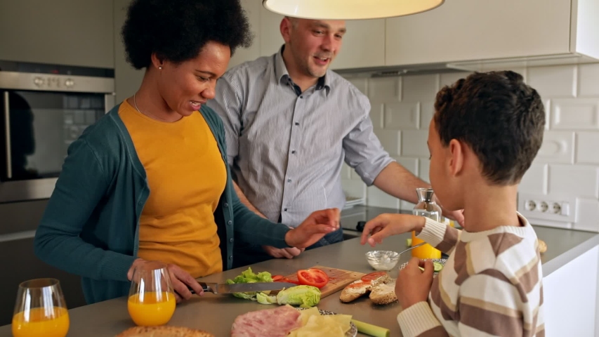 Smiling mixed race family with they son standing in the kitchen preparing sandwich for breakfast at home.