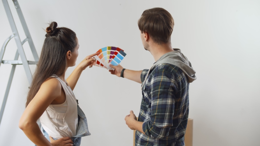 Young happy couple choosing colors for painting wall in new house. Husband and wife holding swatch discussing color of wall in apartment. House decoration and renovation concept