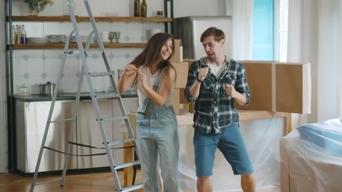 Young beautiful couple dancing at new home around cardboard boxes. Portrait of happy boyfriend and girlfriend having fun celebrating moving in new apartment together