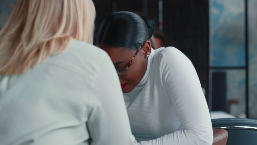 Beautiful young African business coach woman listening to blonde Caucasian colleague speaking at light office meeting. Royalty-Free Stock Footage #1056300593