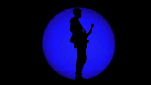 Shadow of unrecognizable bass player in a round beam of blue light. Musician playing a bass guitar in a cloud of haze