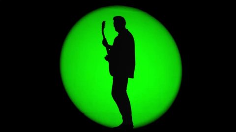 Shadow of an unrecognizable guitarist in a round beam of green light. Musician playing a rhythm guitar