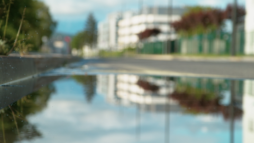 SLOW MOTION, LOW ANGLE, CLOSE UP, DOF: Unrecognizable woman in brand new yellow rubber boots jumps into the glassy puddle on the sidewalk. Carefree young woman in rain boots jumps into the big puddle.
