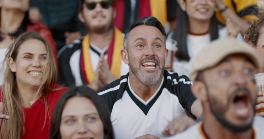 Crowd of spectators cheering at sports event, man holding a glass of beer. Germany football team supporters actively jumping and chanting in crowd.
 Royalty-Free Stock Footage #1056301883