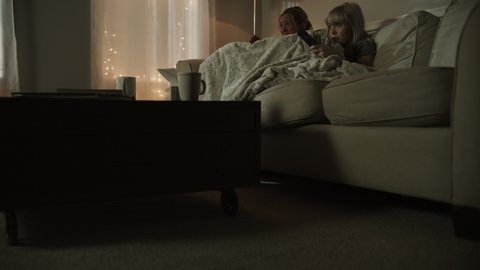 Tilt up to mother and daughter on sofa watching scary movie at night / Cedar Hills, Utah, United States