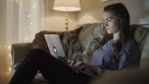 Girl sitting on sofa eating snack and using laptop at night / Cedar Hills, Utah, United States