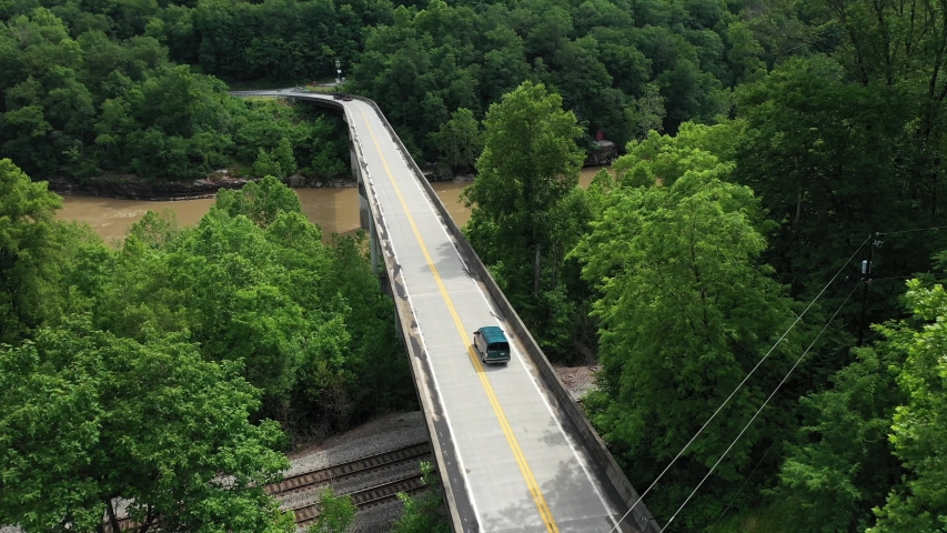 Following Aerial View of Dark Van on Bridge Crossing River and Railway in Countryside of West Virginia, USA, Cinematic Drone Shot