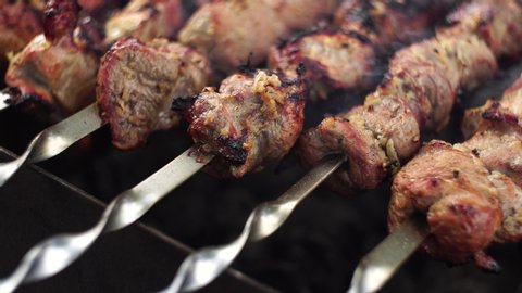 Close up shot of appetizing hot shish kebab on metal skewers prepares on the coals outdoors. Grilling shashlik on barbecue grill