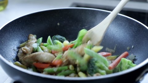 Chicken stir-fry in a pan cooking with wooden spoon, asian paleo keto food