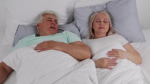 Mature woman pinching nose of snoring husband in bed