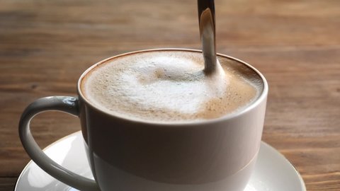Stirring of tasty cappuccino with spoon in cup, closeup