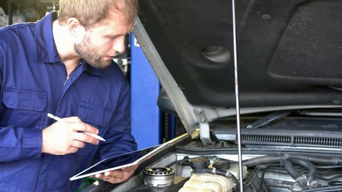 Auto mechanic checking suspension of a lifted car. Experience car service technician working at the garage. Mechanic repairing car at workshop.