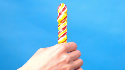 Close up of female hands. In a female hand a candy lollipop, on the other hand, a woman imitates masturbation. Blue simple background