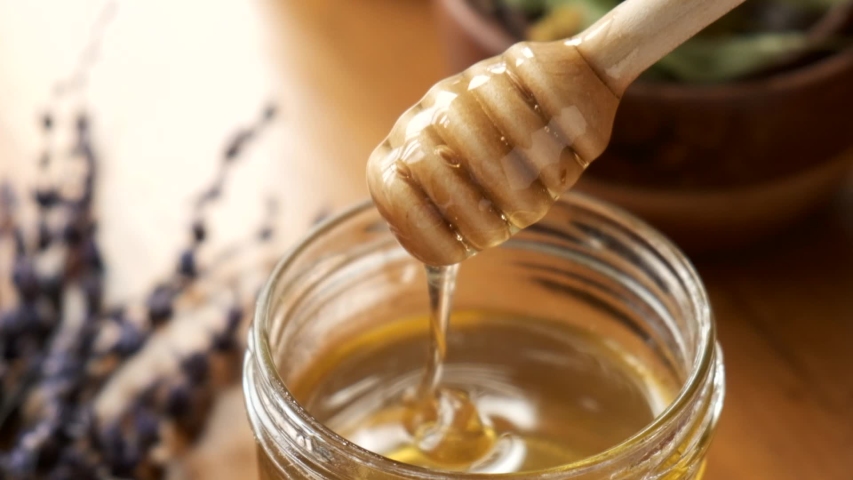 Liquid organic raw honey in glass jar with wooden honey dipper. Slow motion of golden honey flowing in a jar Royalty-Free Stock Footage #1056319037