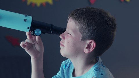 Close up face of curious kid using telescope to explore moon surface. Little boy stargazing at night with a telescope to see galaxy. Young child watching stars through a telescope at night.
