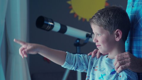 Little boy and old man standing near window near and pointing comet. Happy grandson watching shooting stars during night with grandfather. Child indicates something to grandpa outside the window.