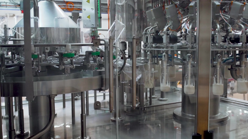 Rotating transporter is pouring fresh milk into bottles. Automated process of filling bottles with milk. Plastic bottles are moving along the conveyor for filling Royalty-Free Stock Footage #1056320300