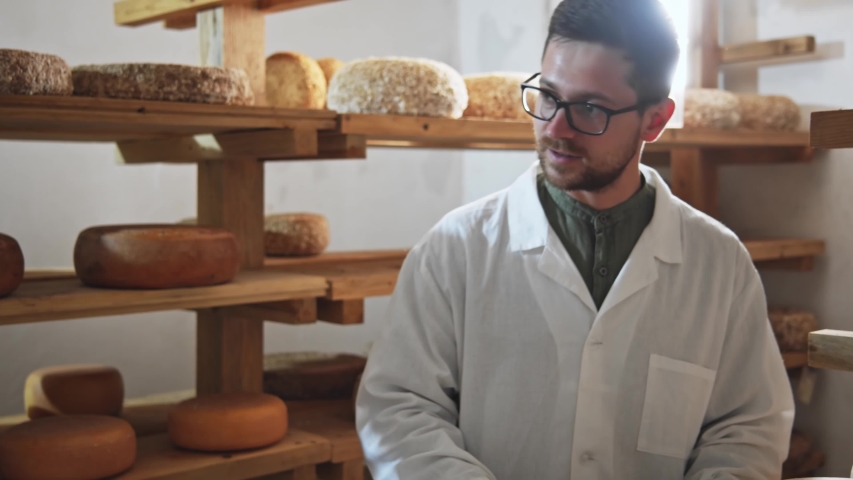 Two farm workers checking ready fresh cheese in small dairy factory on beautiful sunny day. Cheesemaker in milky farm warehouse. Dairy production. Online delivery. Traditional cooking courses. 4K.