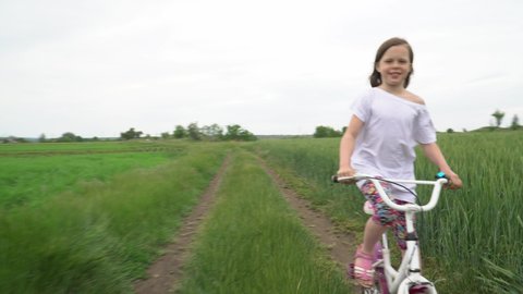 A little girl rides a bicycle on a scenic rural road.