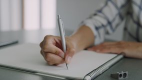 Front view shot of a woman’s hands drawing a line on an a4 sketch book with a blue inked silver office pen, placed on top of an office type table surrounded by utensils. - Powered by Shutterstock - Get 15% off with code: PIKWIZARD15