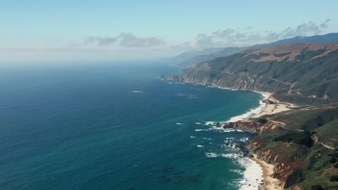 Most scenic stretch of undeveloped coastline in USA, known as Big Sur. 4K Stunning aerial view over the rocky ocean coast. Beautiful ocean water of various shades of blue meets the mountains shore.