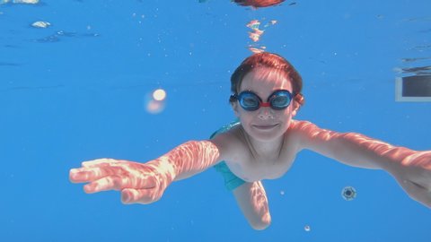 Child enjoying summer vacation. Happy fun loving boy jumping and diving into swimming pool at a pool party in summer sunny day. Slow motion. Underwater view