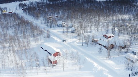 Flight over scandinavian village at Swedish Norwegian border. Beautiful landscape of winter mountains. Aerial view. Car drive in the village on snow road. Sunny cold day, clear air, very white snow