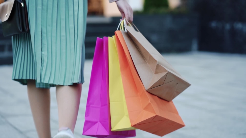 young girl in skirt and with shopping bags looking at the window of next store. Slow motion, back view. Royalty-Free Stock Footage #1056328856