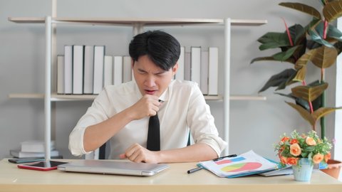 Asian businessman tired yawning while working at office, feeling sleepy while working on laptop, insomnia, exhaustion, stress, fatigue, overwork, sleep disorder concepts